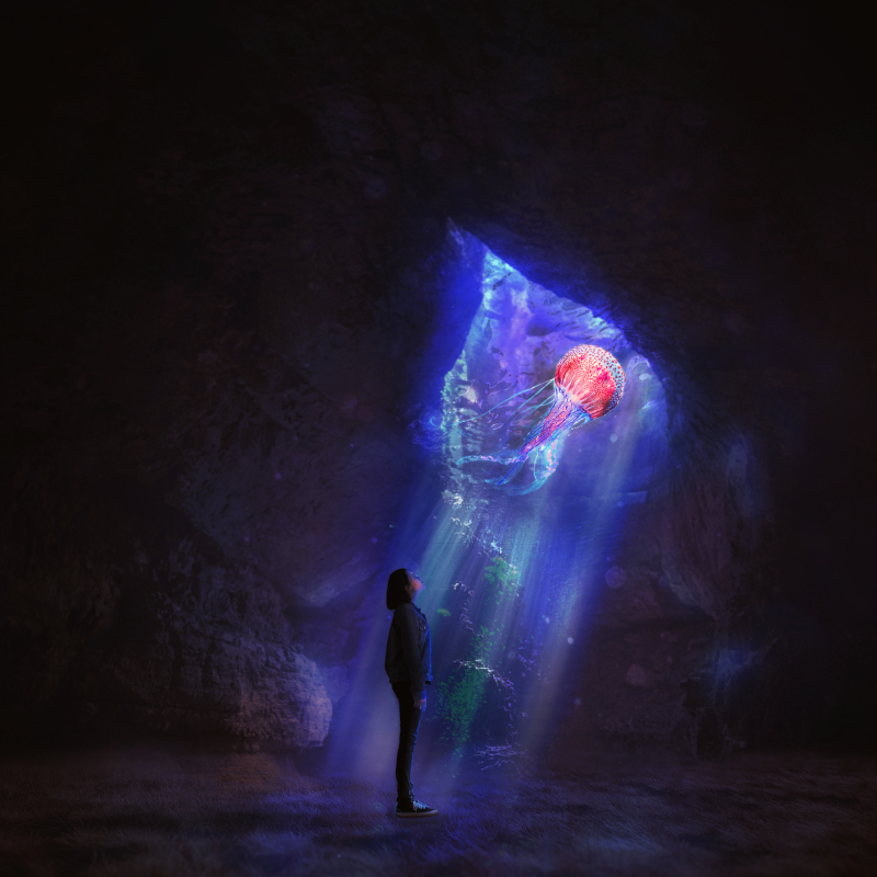 Diver facing a glowing jellyfish in a sea cave